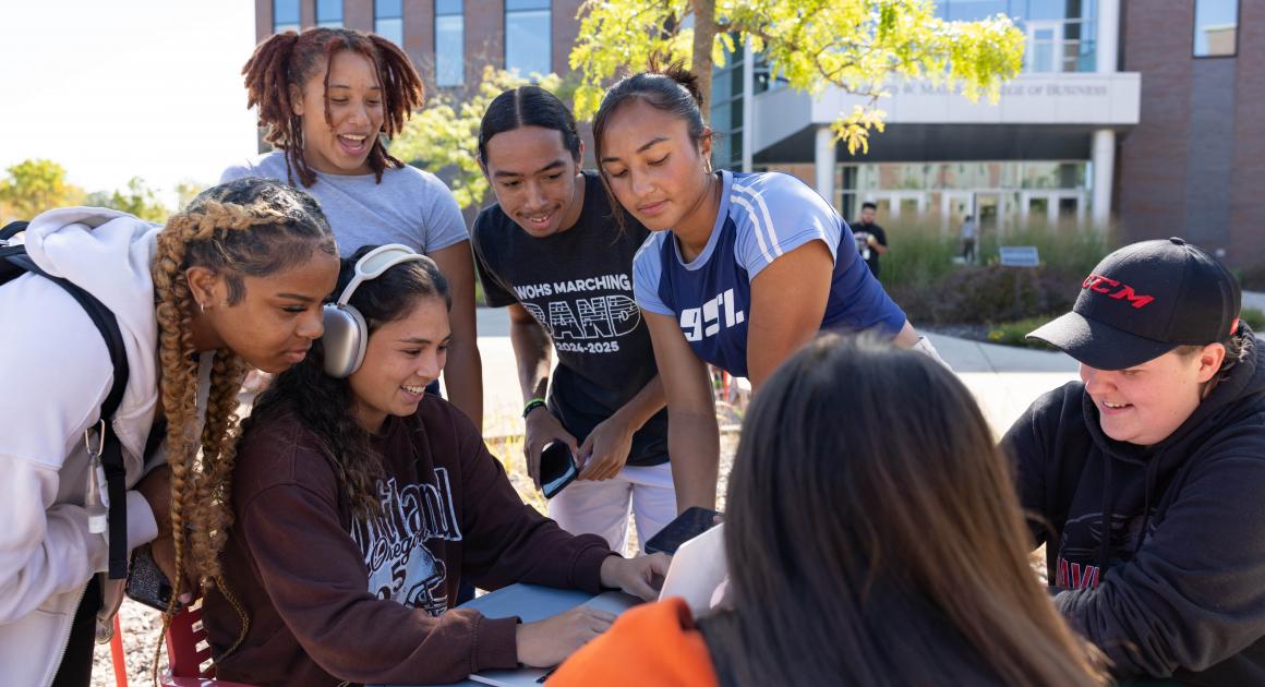 A group of students outside gathered around a table by the College of Business